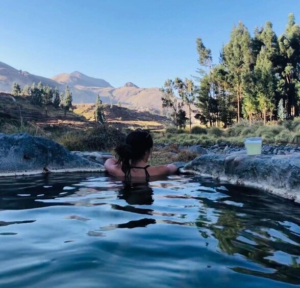 A person relaxing in a natural hot spring surrounded by mountains and trees. 3