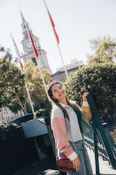 A person standing in front of a clock tower with flags, holding a green bag. 2