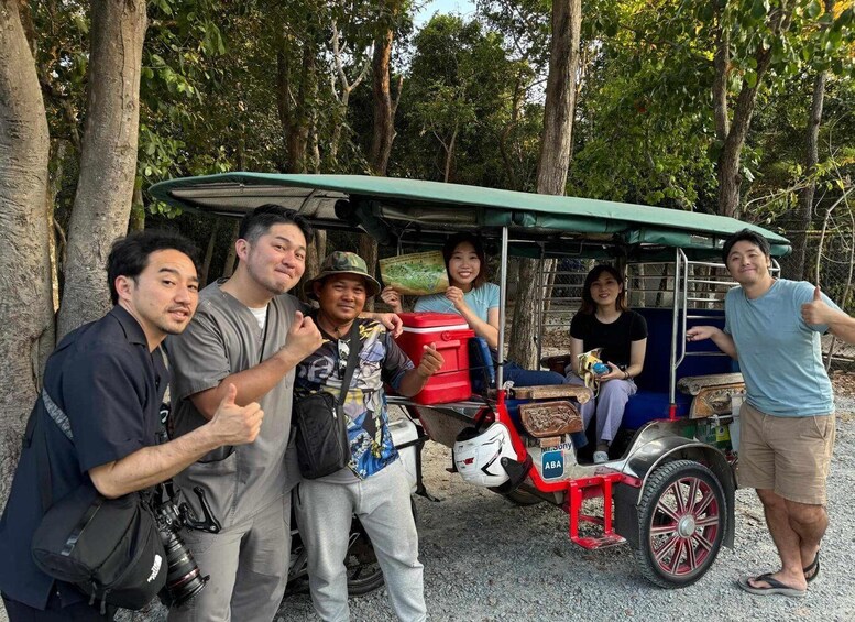 A group of people posing with a three-wheeled vehicle in a forested area. 1