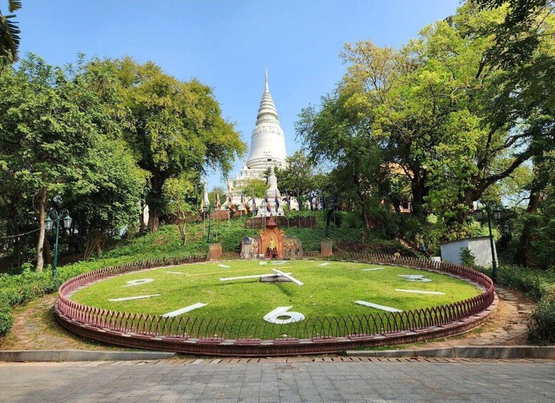 A white stupa surrounded by lush greenery and a circular garden with a fence. 2