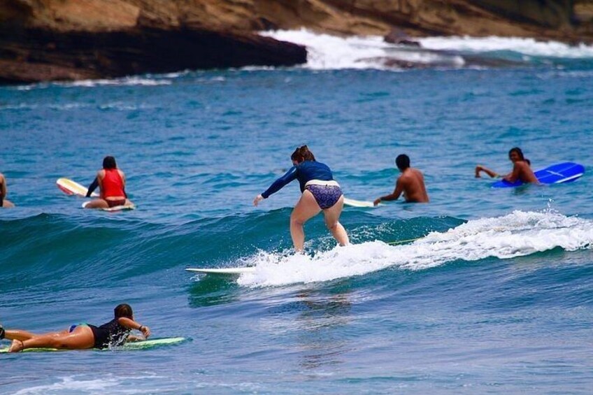 People surfing on waves at a beach with rocky cliffs in the background. 2