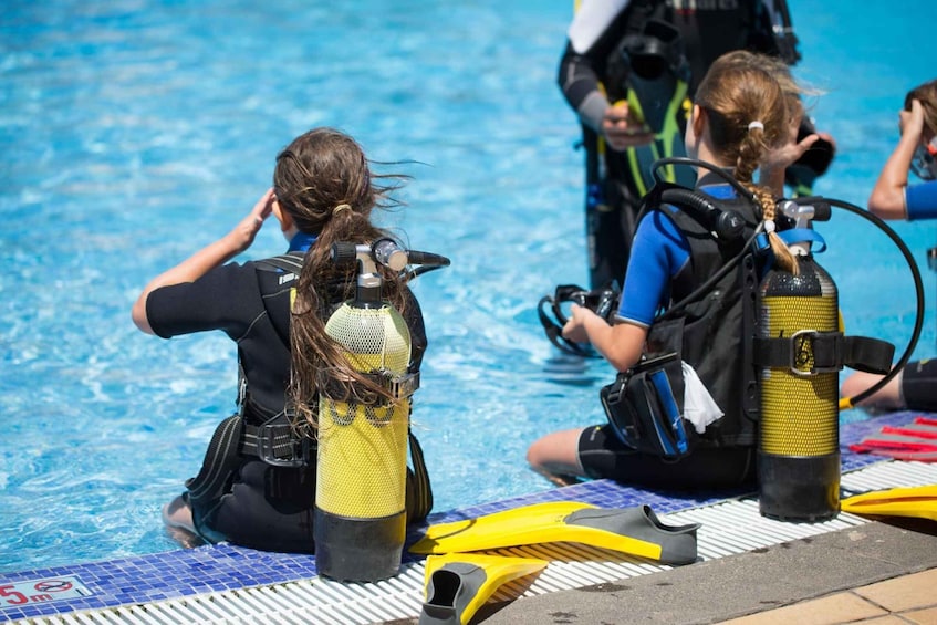 To personer i dykkerudstyr sidder på kanten af en pool. 5