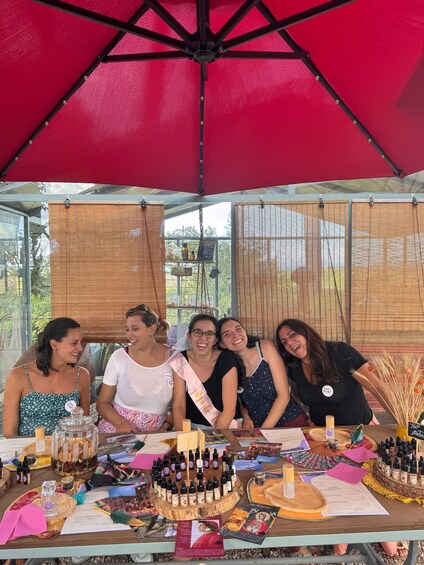 A group of people at a table with various items including a cake, bottles, and papers. 3