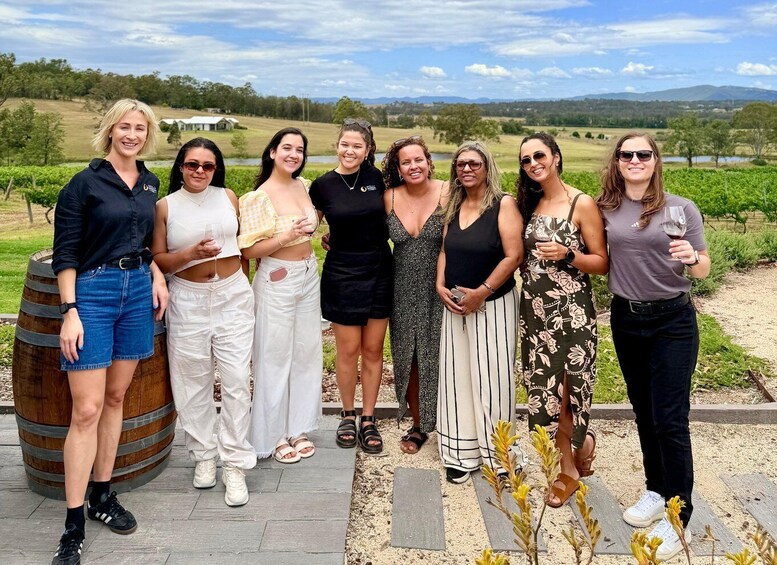 A group of people standing outdoors with a vineyard and hills in the background. 5