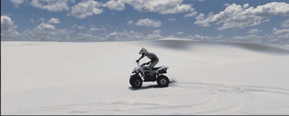 A person riding a quad bike on a snow-covered dune. 1