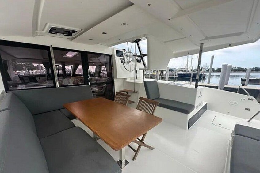 A boat interior with a wooden table, cushioned seating, and windows overlooking the water. 5