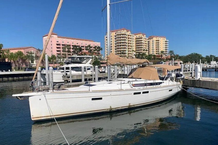 Un voilier blanc est amarré dans une marina, avec des bâtiments en arrière-plan. 1