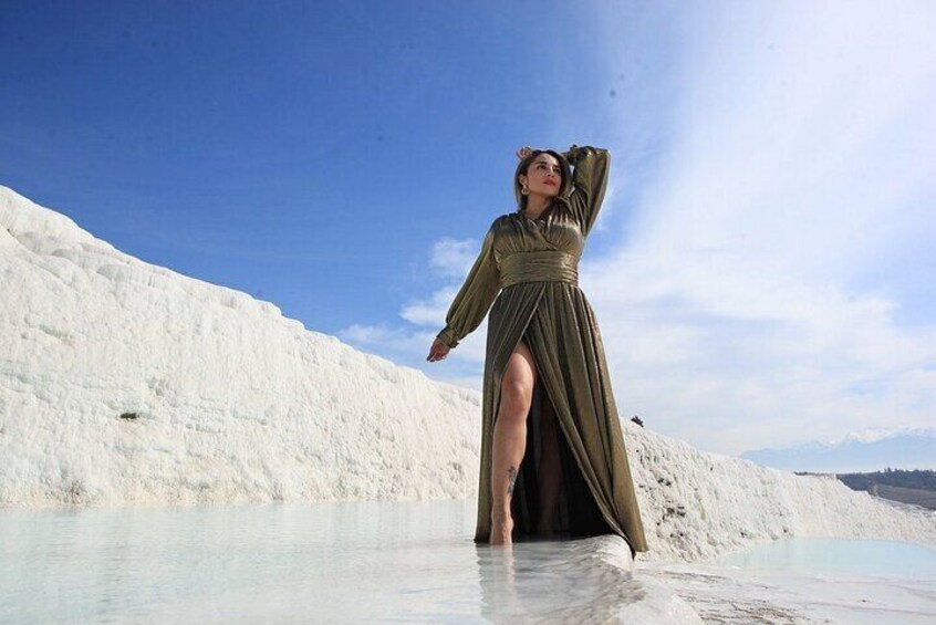 A person in a long dress standing on a white, textured surface with a clear sky in the background. 3