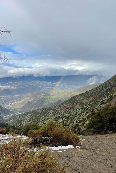 A mountainous landscape with a rainbow, snow patches, and a river valley. 3