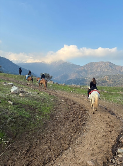 A dirt path with riders on horses, surrounded by mountains and greenery. 2