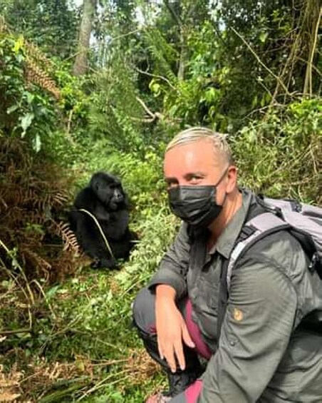 A person crouching in a forest with a gorilla in the background. 2