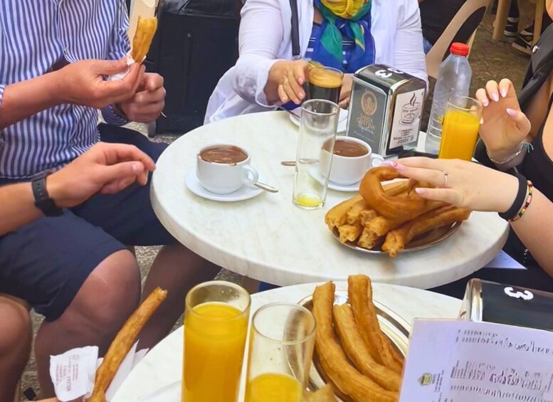 People sitting at a round table with coffee, churros, and orange juice. 2
