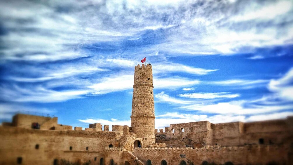 A historic stone tower with a flag, surrounded by ancient walls under a partly cloudy sky. 2