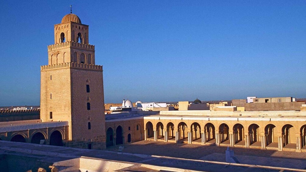 A historic tower with a dome, surrounded by a courtyard with arches and a clear blue sky. 4