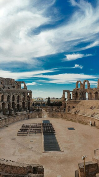 An ancient amphitheater with stone ruins and a central stage. 3