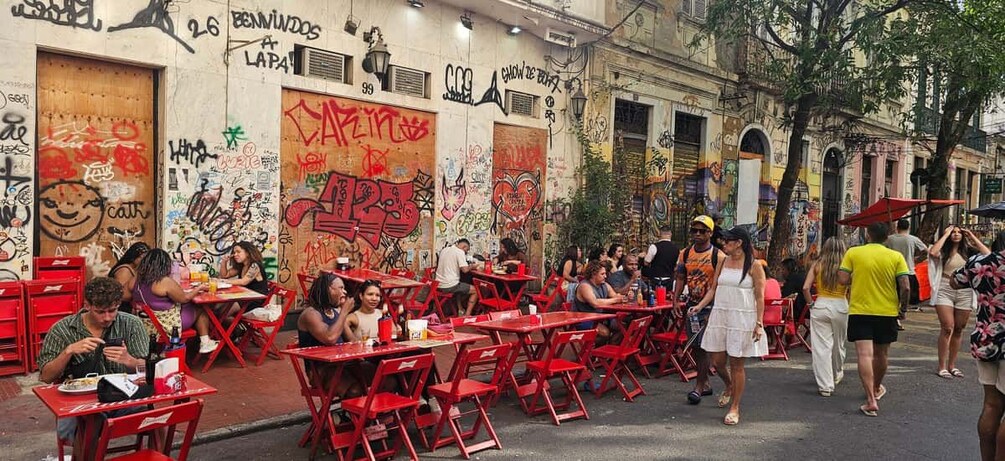 Outdoor dining tables and chairs, graffiti on walls, and people walking by. 5