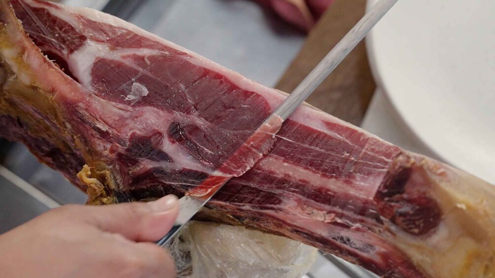 A person slicing a large piece of meat with a knife. 5