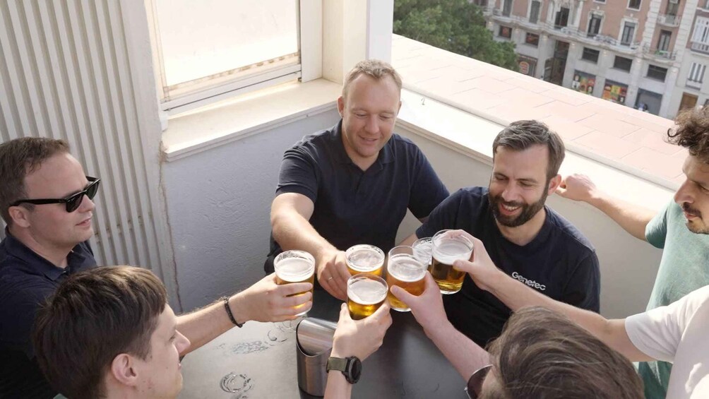 A group of people toasting with beer glasses on a balcony. 3