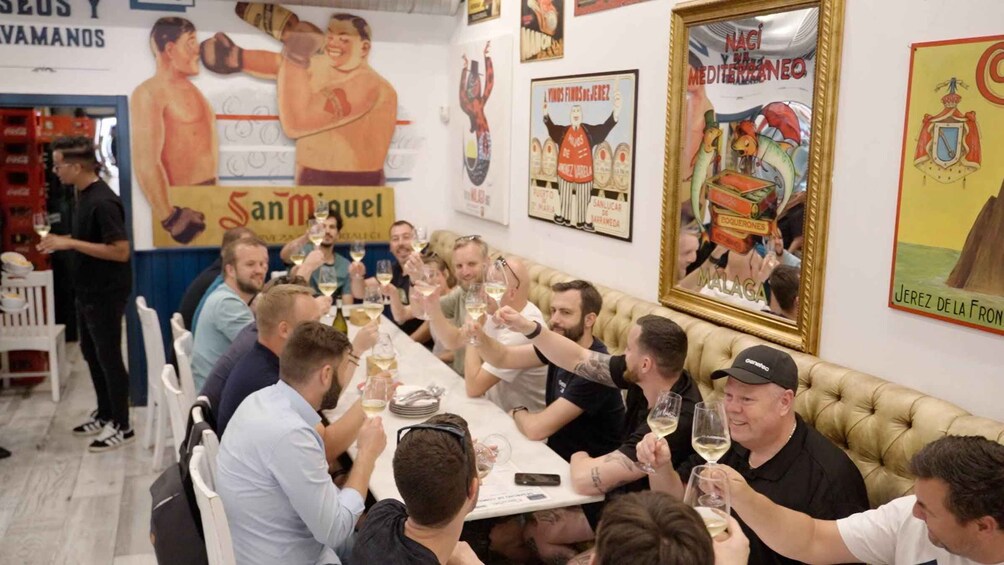 A group of people toasting with wine glasses at a restaurant with a mural of boxers and a framed picture of a bull. 2