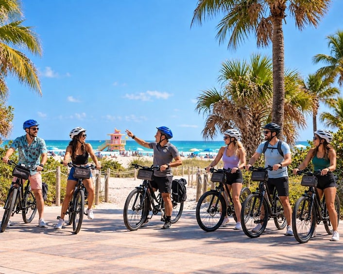 A group of people on bicycles along a coastal walkway with palm trees and a beach in the background. 2