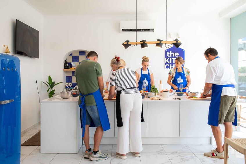 A group of people in a kitchen with a blue sign that reads 'the KIT CH'. 3
