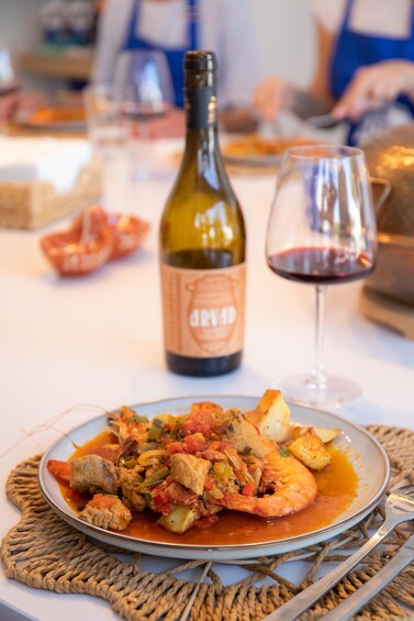 A plate of food with a bottle and a glass of red wine on a table. 4