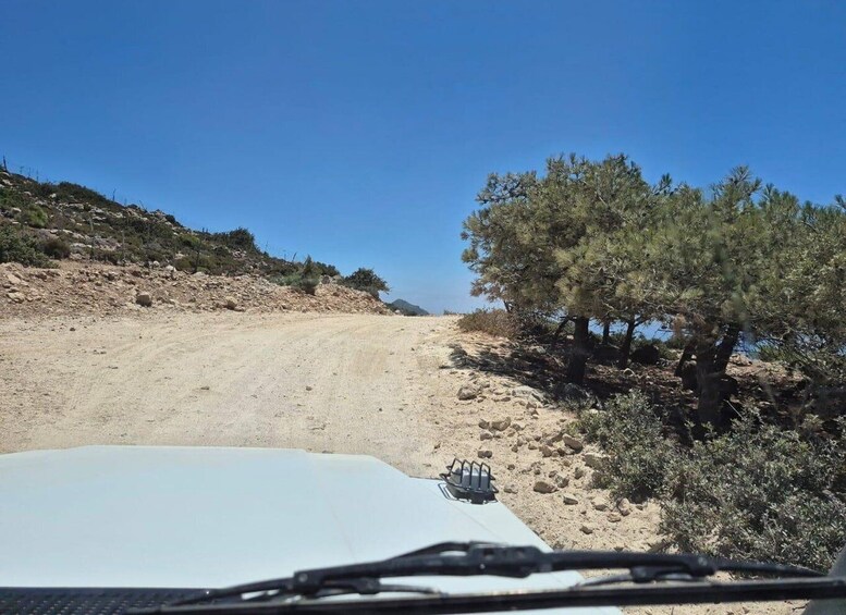 A white vehicle on a dirt road with sparse vegetation and a clear blue sky. 3