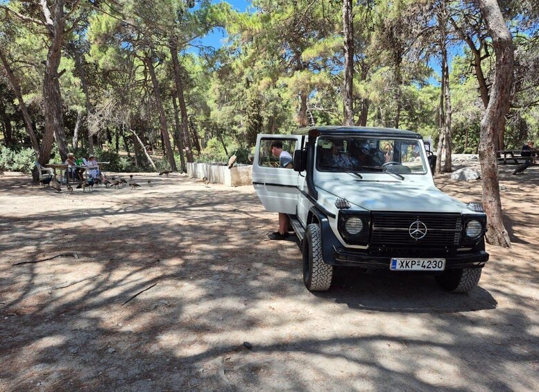 A Mercedes-Benz G-Class SUV parked in a wooded area with picnic tables and people in the background. 5