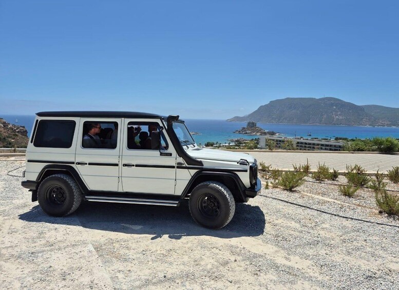 A white SUV parked on a gravel road with a coastal landscape in the background. 1