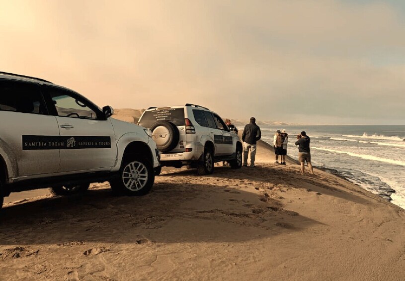 A safari vehicle parked on a beach with people standing nearby. 5