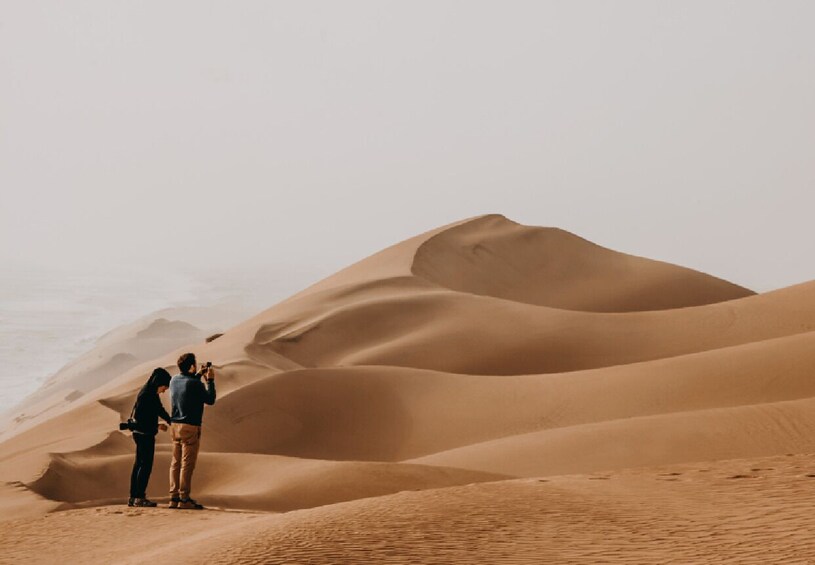 Two people standing on a sandy dune with a desert landscape in the background. 4