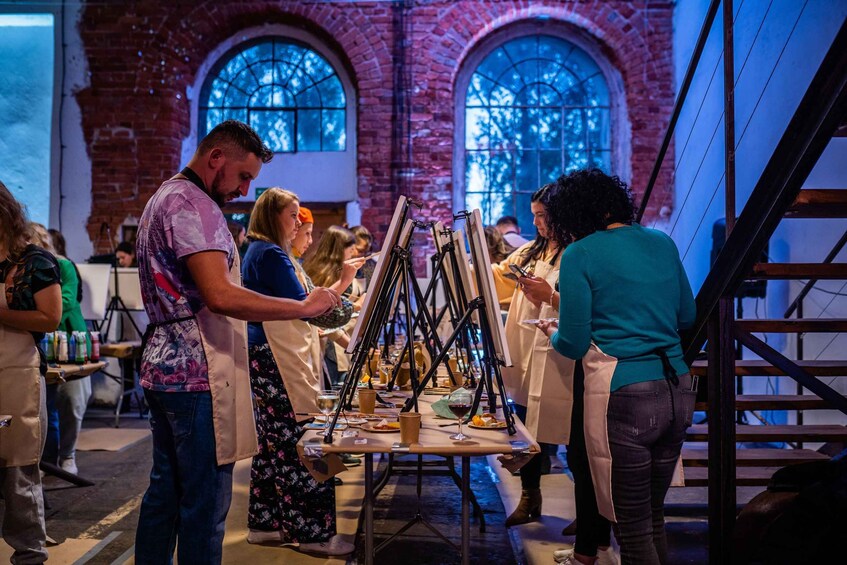People painting in a room with arched windows and brick walls. 5
