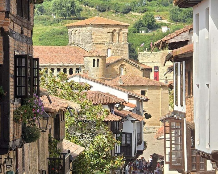 A narrow street with historic buildings, a church, and a crowd of people. 4