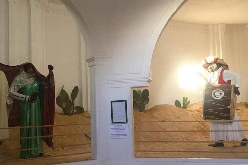 A museum exhibit with a statue of a woman in green and a man playing a drum. 3