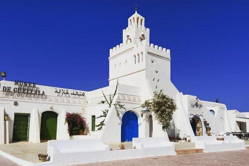 A white building with a blue door and a tower. 1