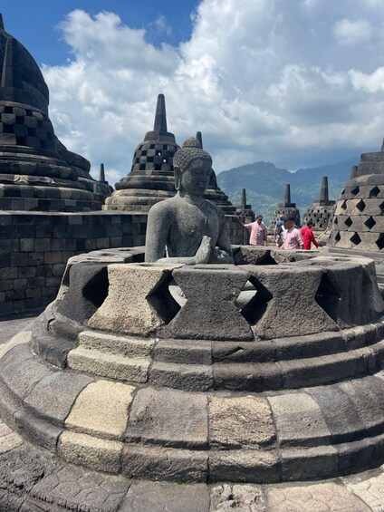 A stone Buddha statue in a temple complex with visitors. 1