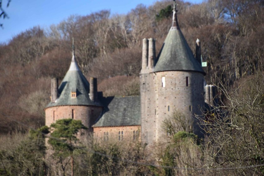 A castle with two towers and a central building, surrounded by trees and hills. 2