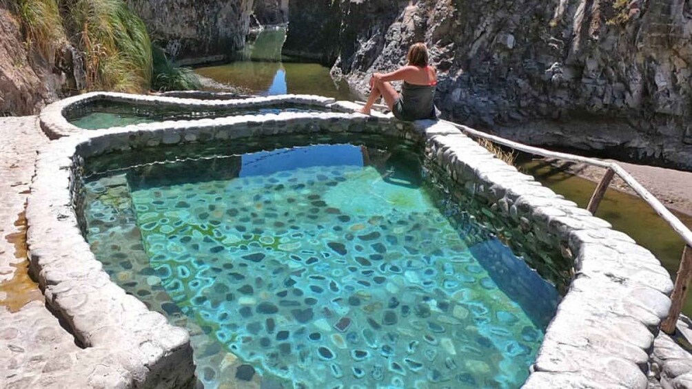 A person sitting by a clear pool with a rocky edge. 5