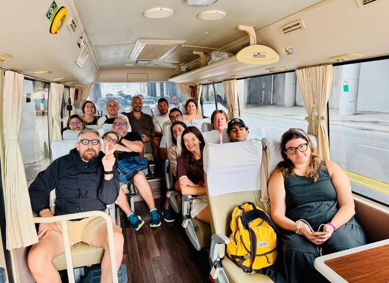 A group of people seated inside a bus, with a cityscape visible through the windows. 3