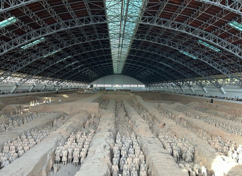 A large open space with a high ceiling and metal framework, filled with numerous stone statues of soldiers. 5