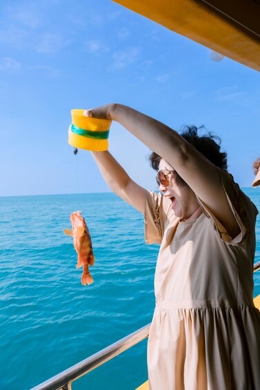 A person on a boat holding a yellow and green bucket, attempting to catch a fish in the water. 1