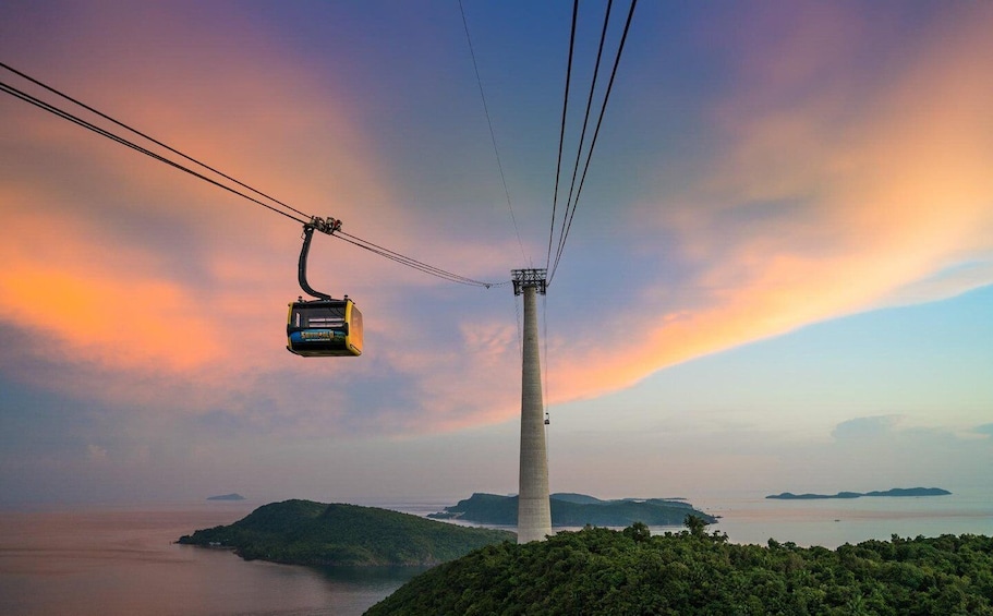 A cable car system with a cable car suspended between two towers, overlooking a coastal landscape with hills and a body of water. 1