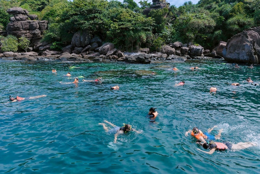People swimming in a clear blue pool surrounded by rocks and greenery. 3