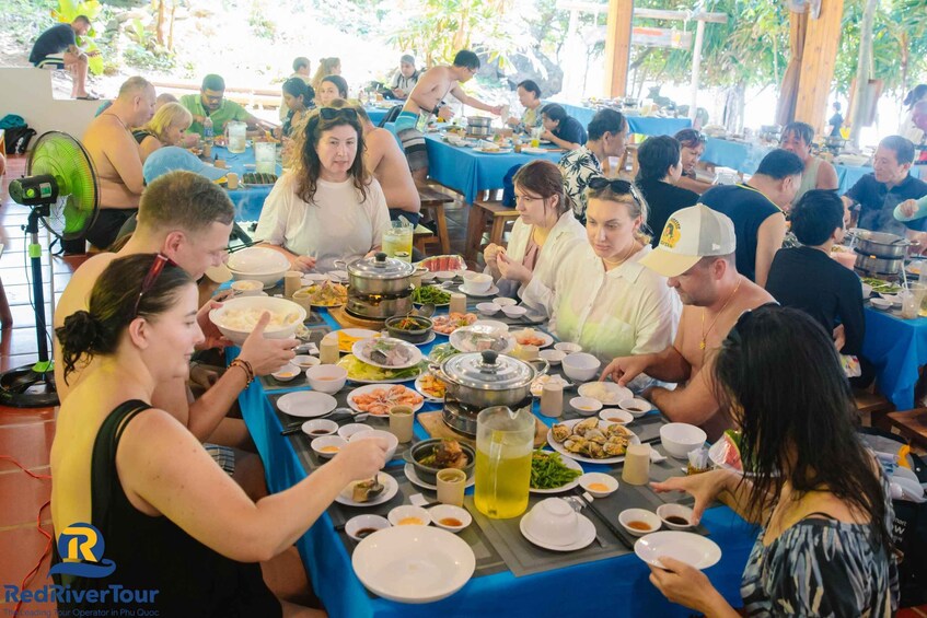 A group of people dining at an outdoor event with various dishes and drinks on tables. 4