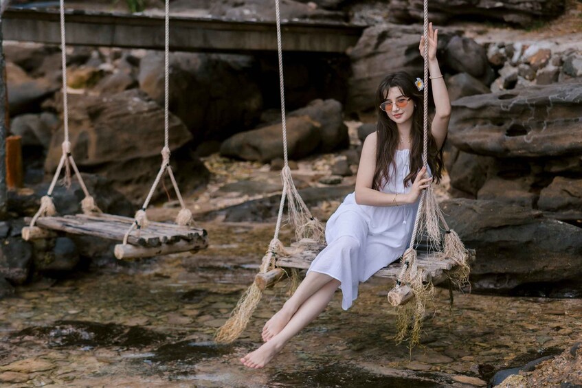 A person sitting on a rope swing over a rocky stream. 5