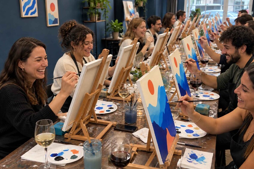 A group of people painting on easels in a well-lit room with art supplies and wine glasses on the tables. 3