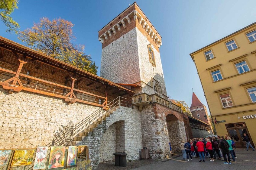 A historic stone tower with a clock, a wooden bridge, and a crowd of people. 4