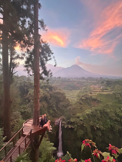 A wooden platform overlooking a waterfall, with a mountain and sunset in the background. 1