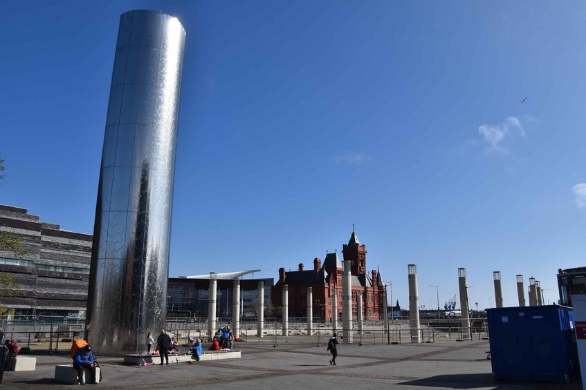 A large metallic cylinder, a historic building, and a modern structure in an open plaza. 4