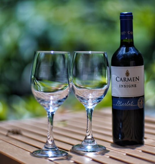 Two empty wine glasses and a bottle of Carmen Insigne Merlot wine on a wooden table. 2